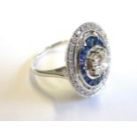 An Art Deco style 18-carat white gold ring set with a 1 carat diamond surrounded by sapphires and