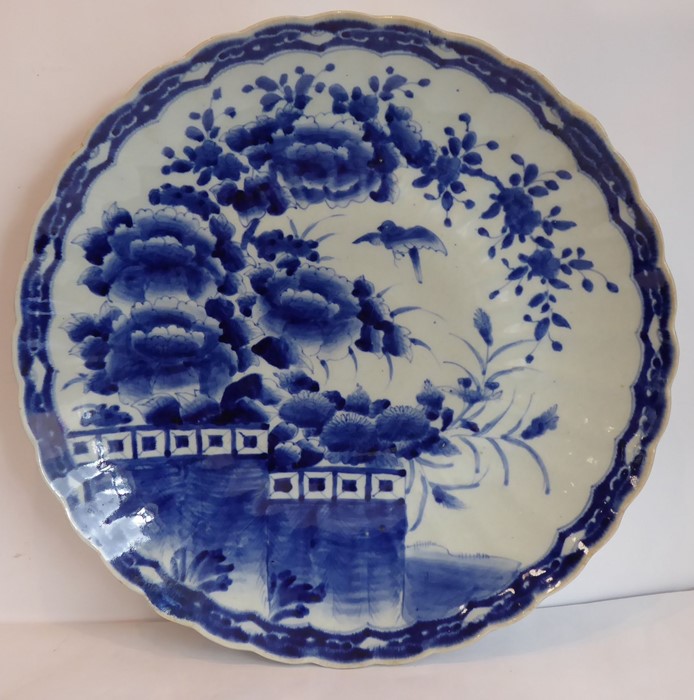 A large Japanese porcelain charger, scalloped edge and hand decorated in underglaze blue with a