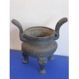 An Oriental patinated bronze tripod censer, the two pierced outward facing handles above three