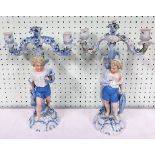 Two 19th Century continental porcelain two branch candelabra each supported by a young boy, with one