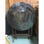 A heavily carved tilting oriental table top with junks on sea on a simple base diameter 62cm