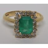 A marked 750 gold diamond and emerald cluster ring, with the step cut emerald measuring