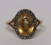 An oval faceted lemon citrine cocktail ring with a seed pearl surround on an unmarked gold (