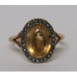 An oval faceted lemon citrine cocktail ring with a seed pearl surround on an unmarked gold (