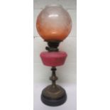 Victorian brass oil lamp with a pink glass reservoir and a dark orange shade, with floral