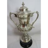A Victorian silver trophy and lid with fancy scroll handles and a heavily embossed body decorated