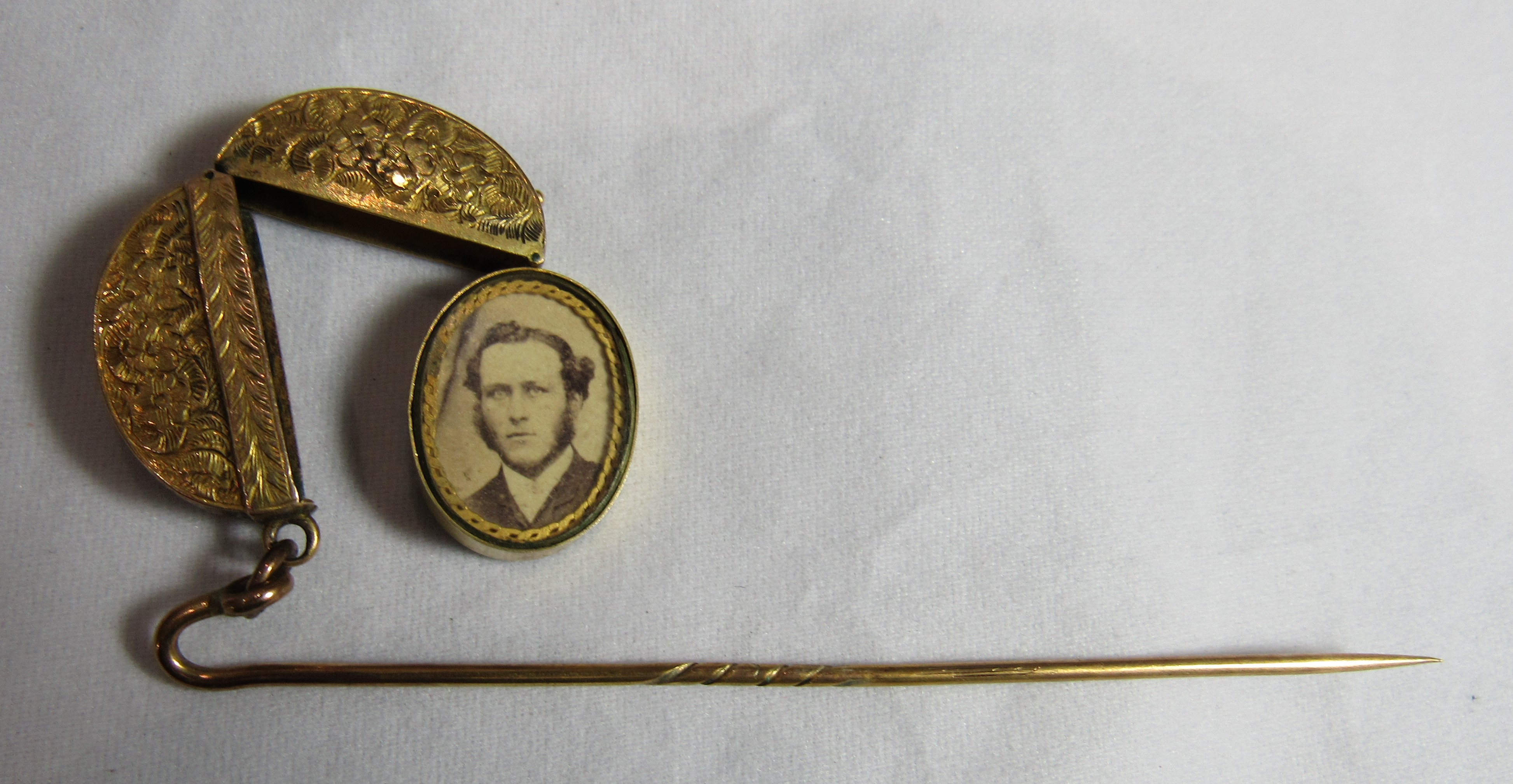 An unmarked gold or gilt hat pin with an attached oval locket with floral engraving and opens to - Image 2 of 3