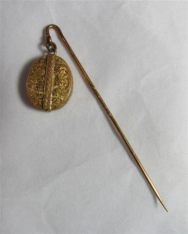 An unmarked gold or gilt hat pin with an attached oval locket with floral engraving and opens to