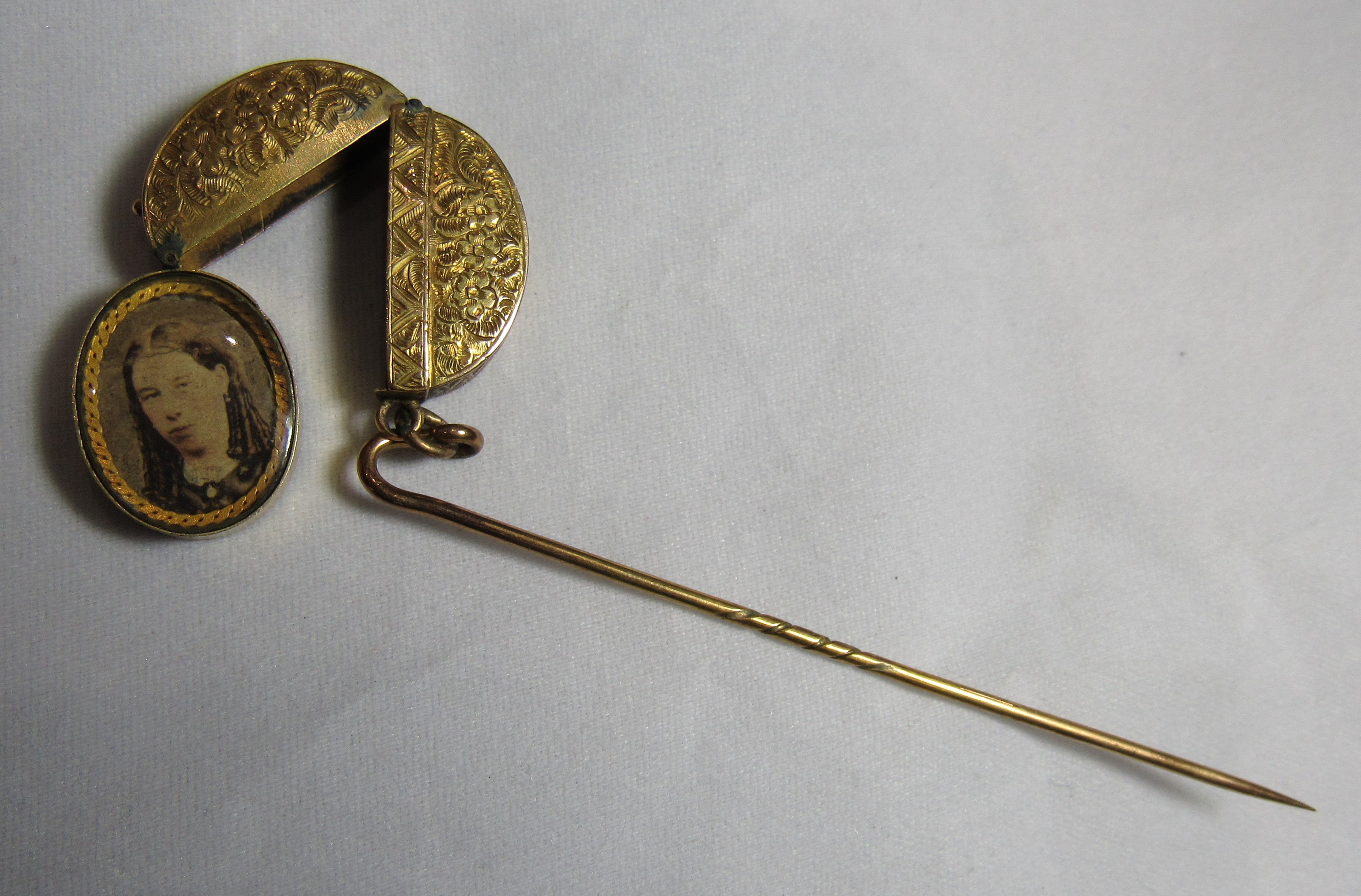 An unmarked gold or gilt hat pin with an attached oval locket with floral engraving and opens to - Image 3 of 3