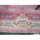 A large predominantly rose pink rectangular rug of oriental design with fringed ends, approx.