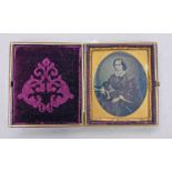 GILT METAL FRAMED OVAL AMBROTYPE OF A MIDDLE AGED WOMAN WITH FRILLED COLLAR OF A TABLE WITH A BOOK