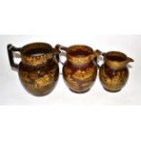 A Graduated Set of Three Nelson Commemorative Brown Glazed Pottery Jugs, circa 1805, printed in