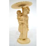 A Japanese Ivory Okimono, Meiji period, as a mother holding a parasol, her child on her back, on