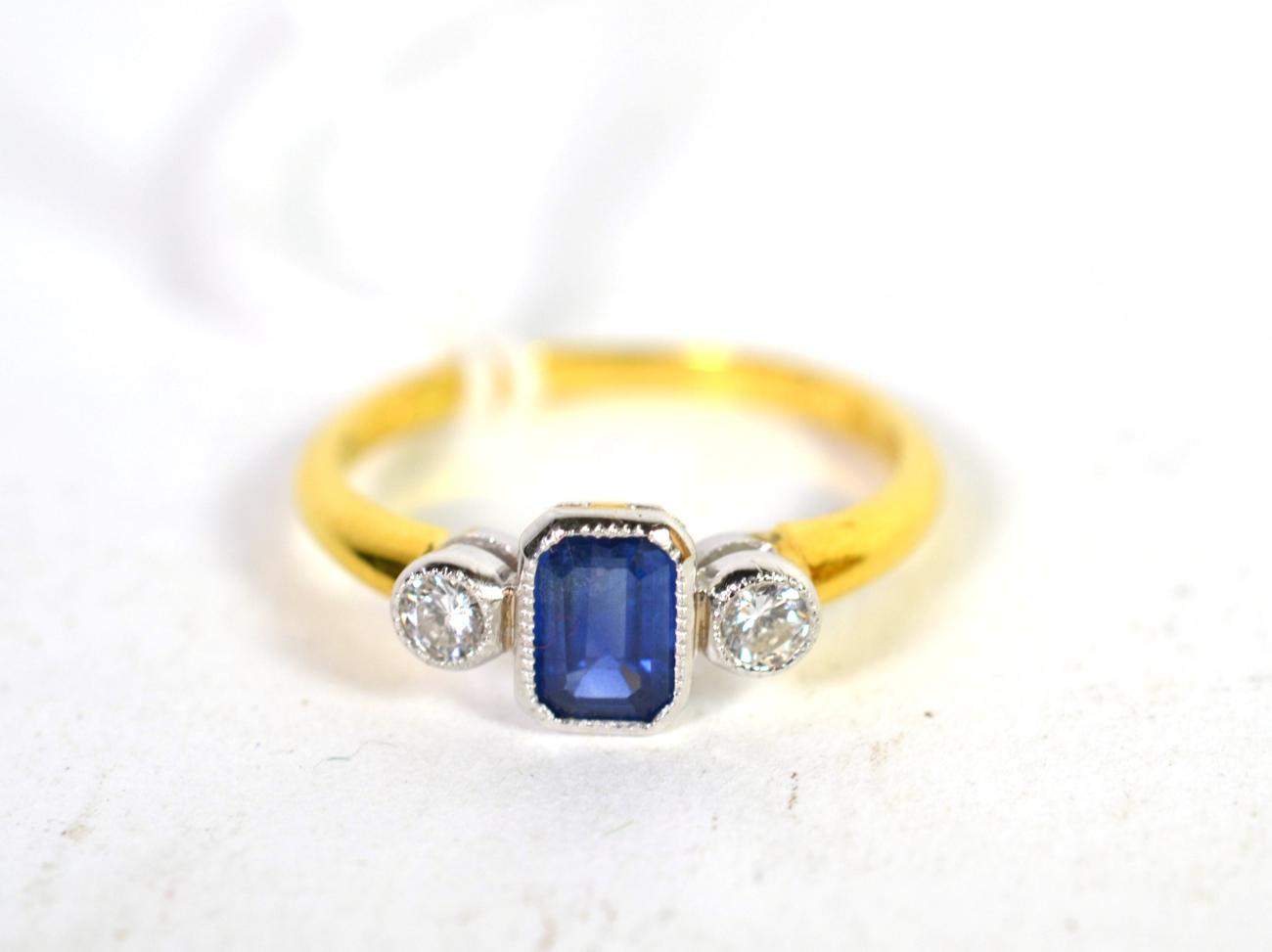 An 18 carat gold sapphire and diamond three stone ring, an emerald cut sapphire spaced by round