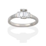 A Platinum Diamond Three Stone Ring, a central emerald-cut diamond in a four claw setting, flanked