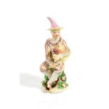 A Longton Hall Porcelain Commedia dell'Arte Figure of Harlequin, circa 1755, sitting playing the