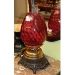 A brass and patinated metal oil lamp with artichoke form ruby glass shade