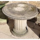 A weathered composition pedestal garden table, the circular top on a fluted column base