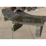 A weathered composition garden bench of curved form, raised on three scroll decorated legs