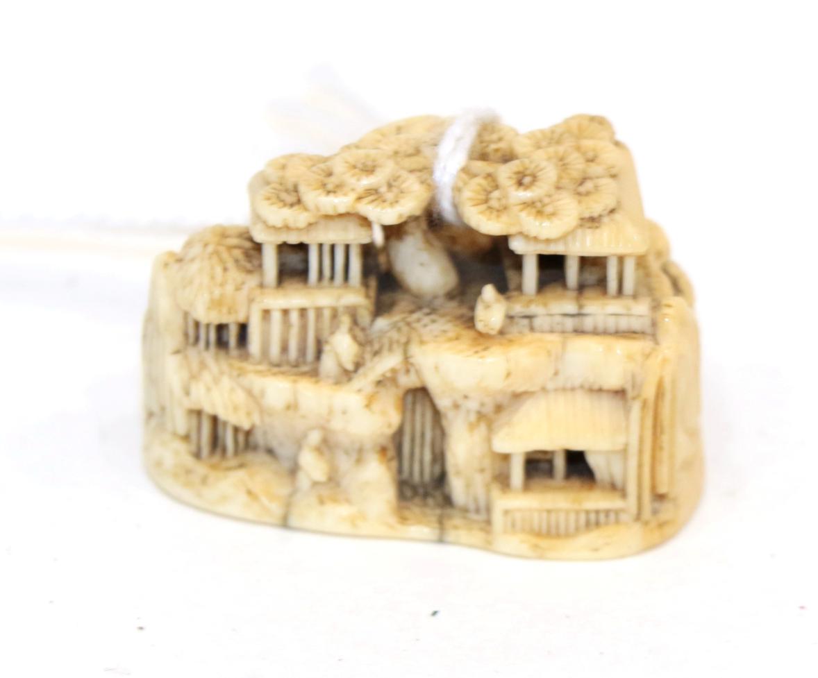 A Japanese Ivory Netsuke, Meiji period, carved as figures and buildings in a rocky landscape,