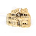 A Japanese Ivory Netsuke, Meiji period, carved as figures and buildings in a rocky landscape,
