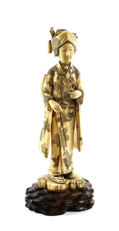 A Japanese Carved Ivory Figure of a Girl, Meiji period, standing in traditional robes holding a