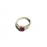 A ruby and diamond ring, an oval cut ruby in a white claw setting, flanked by trilliant cut