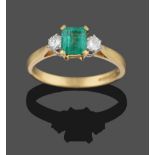 An 18 Carat Gold Emerald and Diamond Three Stone Ring, the emerald-cut emerald in a yellow four claw