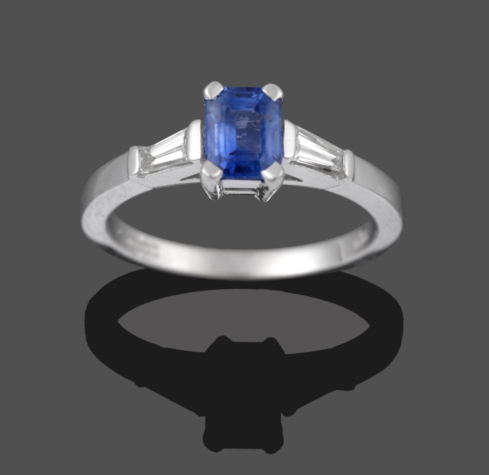 An 18 Carat White Gold Sapphire and Diamond Three Stone Ring, the emerald-cut sapphire in a white