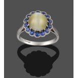 A Cats-Eye Chrysoberyl and Sapphire Cluster Ring, the circular cabochon cats-eye chrysoberyl in a