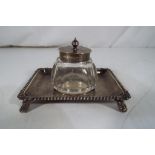 An Edward VII silver hallmarked inkwell stand with gadroon edge raised on four supports with glass