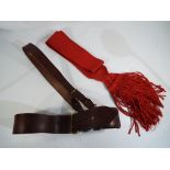 An officer's belt with shoulder strap and red sash.