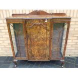 A glass fronted cabinet with decorative carved detailing measuring approximately 115 cm x 120 cm x