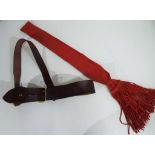 An officers belt with shoulder strap and red sash.