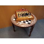 A decorative chess board table raised on three elephant mask supports with faux ivory inlay