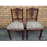 A pair of highly carved dining chairs with upholstered seats.