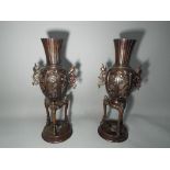 A pair of hot cast bronze twin handled vases on tripod supports,