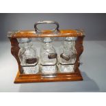 An oak and white metal Tantalus, holdfast by Walker & Hall, fitted with three cut glass decanters,