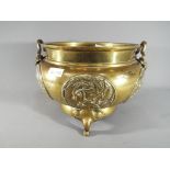A large Oriental brass bowl, raised on three supports, decorated with panels,