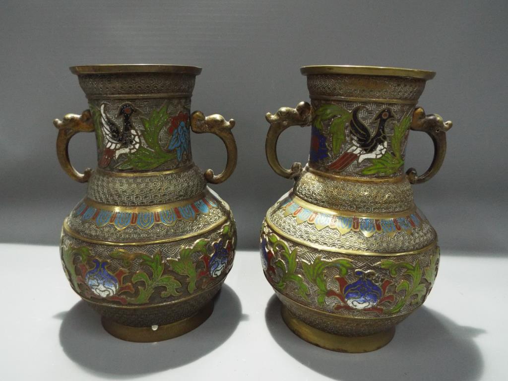 A pair of brass cloisonne twin handled vases depicting birds,