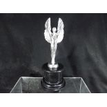 A white metal figure depicting a winged angel mounted on a circular black plinth,