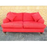 A two seater red upholstered sofa set on casters, approximate height 90 cm x 170 cm x 90 cm.