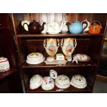 Three shelves containing a quantity of ceramics to include teapots, jelly moulds,