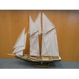 A wooden model of a sailing boat on stand, approximately 88 cm [h] by 90 cm [L].