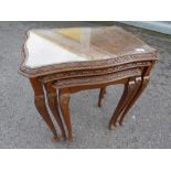 A nest of three glass topped tables with carved decoration,