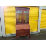 A bookcase having glazed doors and three shelves over a bureau base,