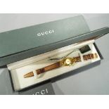 Gucci - a designer Gucci wristwatch with leather Gucci strap, yellow metal coloured Gucci face,