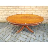 An oval topped, tilt top coffee table on castors, approximately 50 cm x 117 cm x 77 cm.