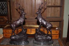 Pair of bronze models of stags standing on rocky outcrops, raised on marble plinths,