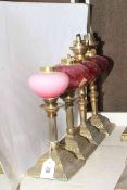 Four brass oil lamp bases with ruby glass reservoirs